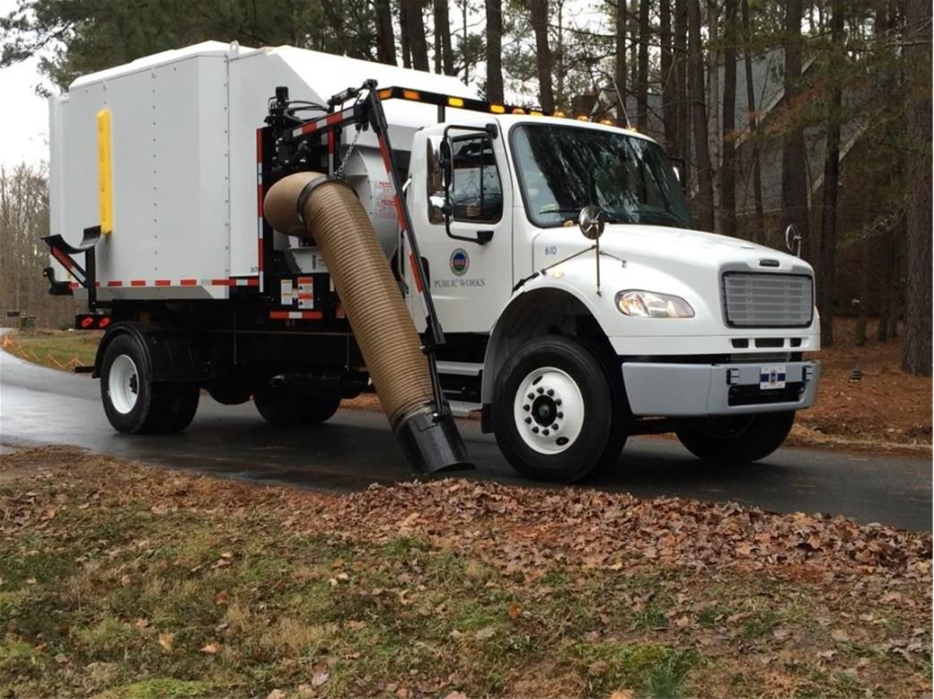 Picture shows leaf vacuum truck collecting loose leaves along the side of a roadway. 
